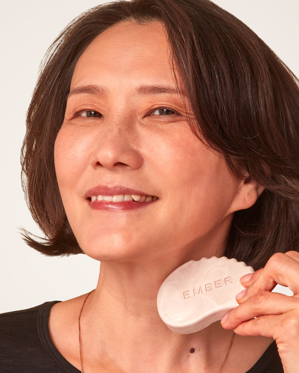 A woman smiles broadly as she holds the 3-in-1 Sculpt & Glow bar to her face.