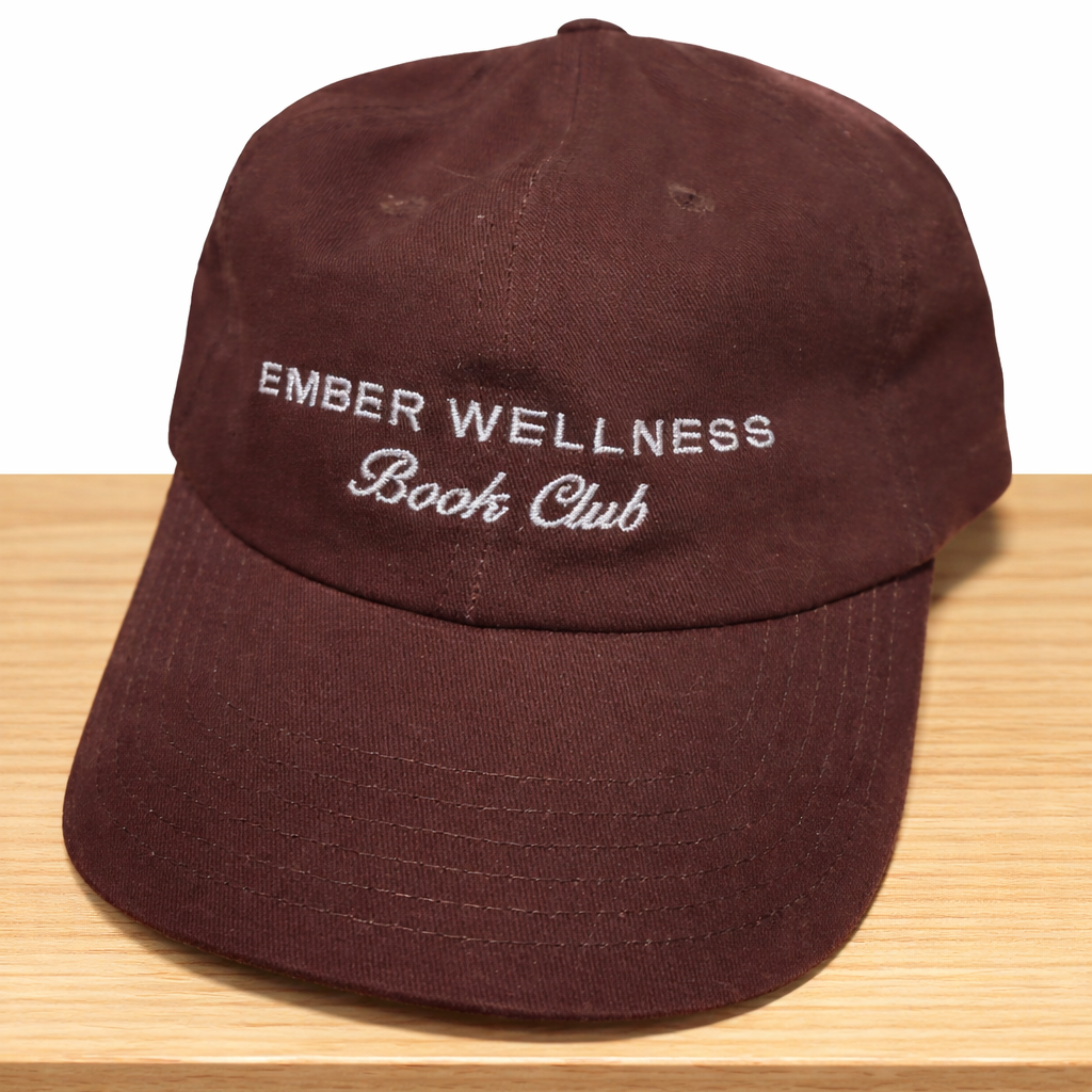Brown cap with 'Ember Wellness Book Club' text on a wooden surface