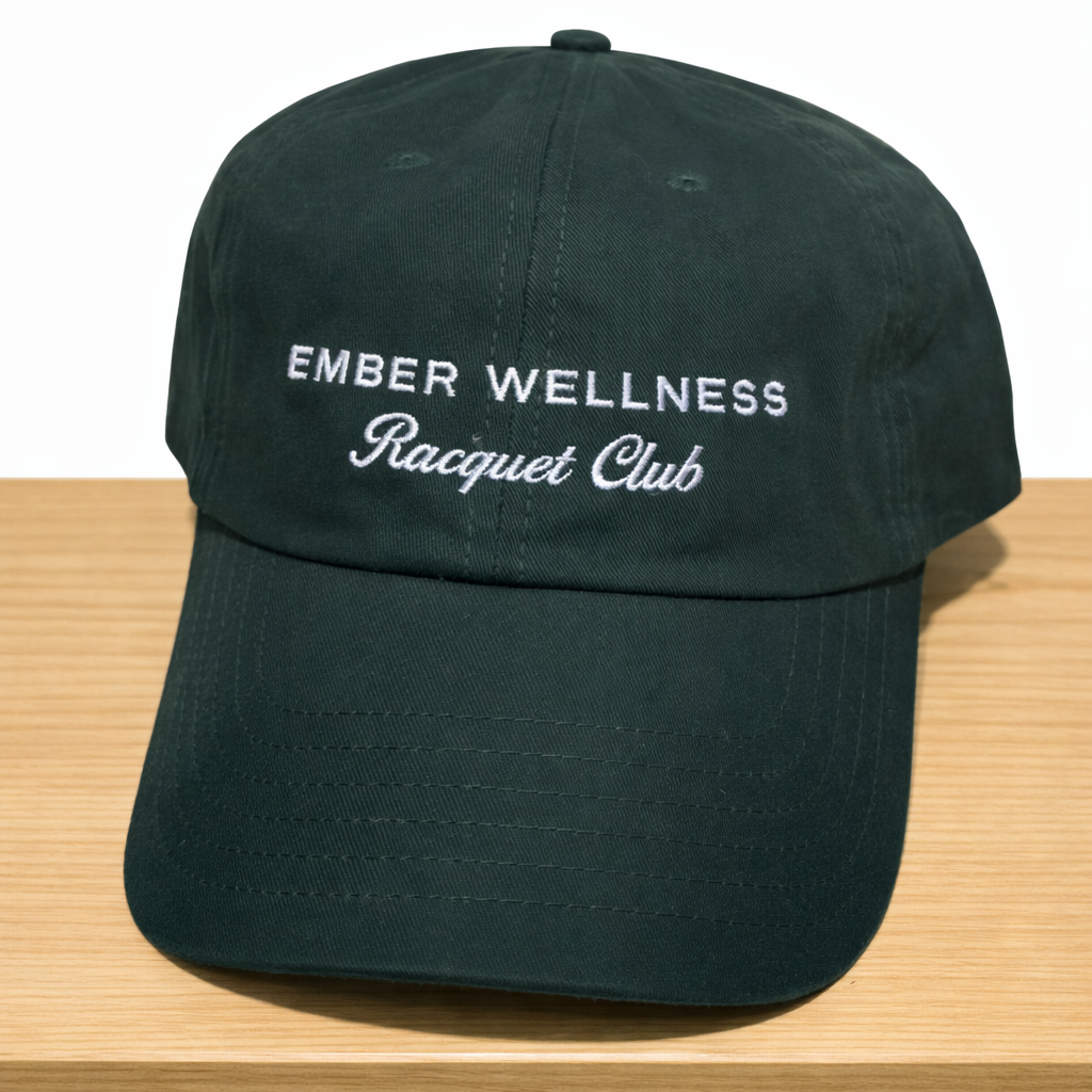 Black cap with 'Ember Wellness Racquet Club' text on a wooden surface